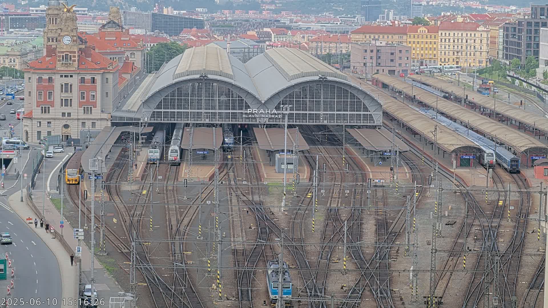 A large train station with numerous tracks and platforms, multiple trains, and surrounding city buildings under an overcast sky.
