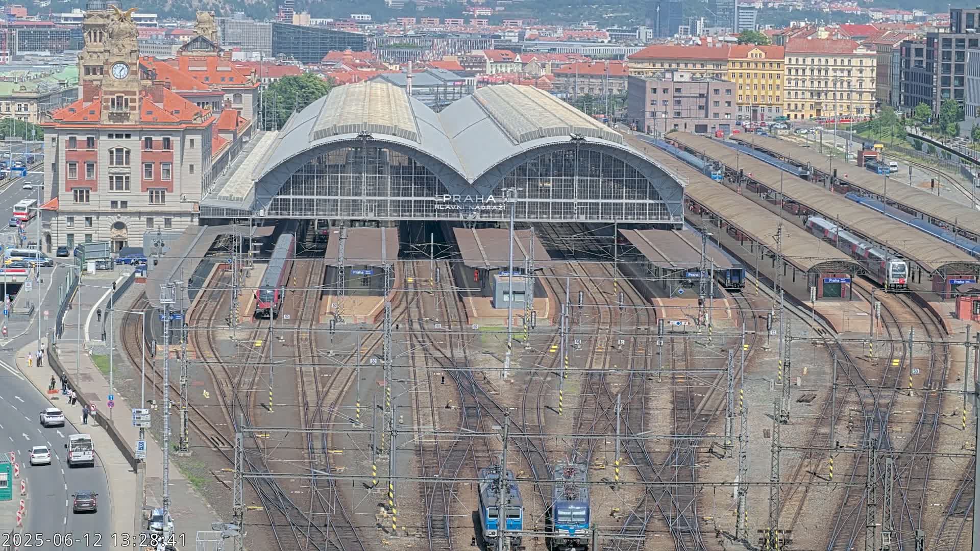 A large train station with numerous tracks and several trains, viewed from above on a clear day.
