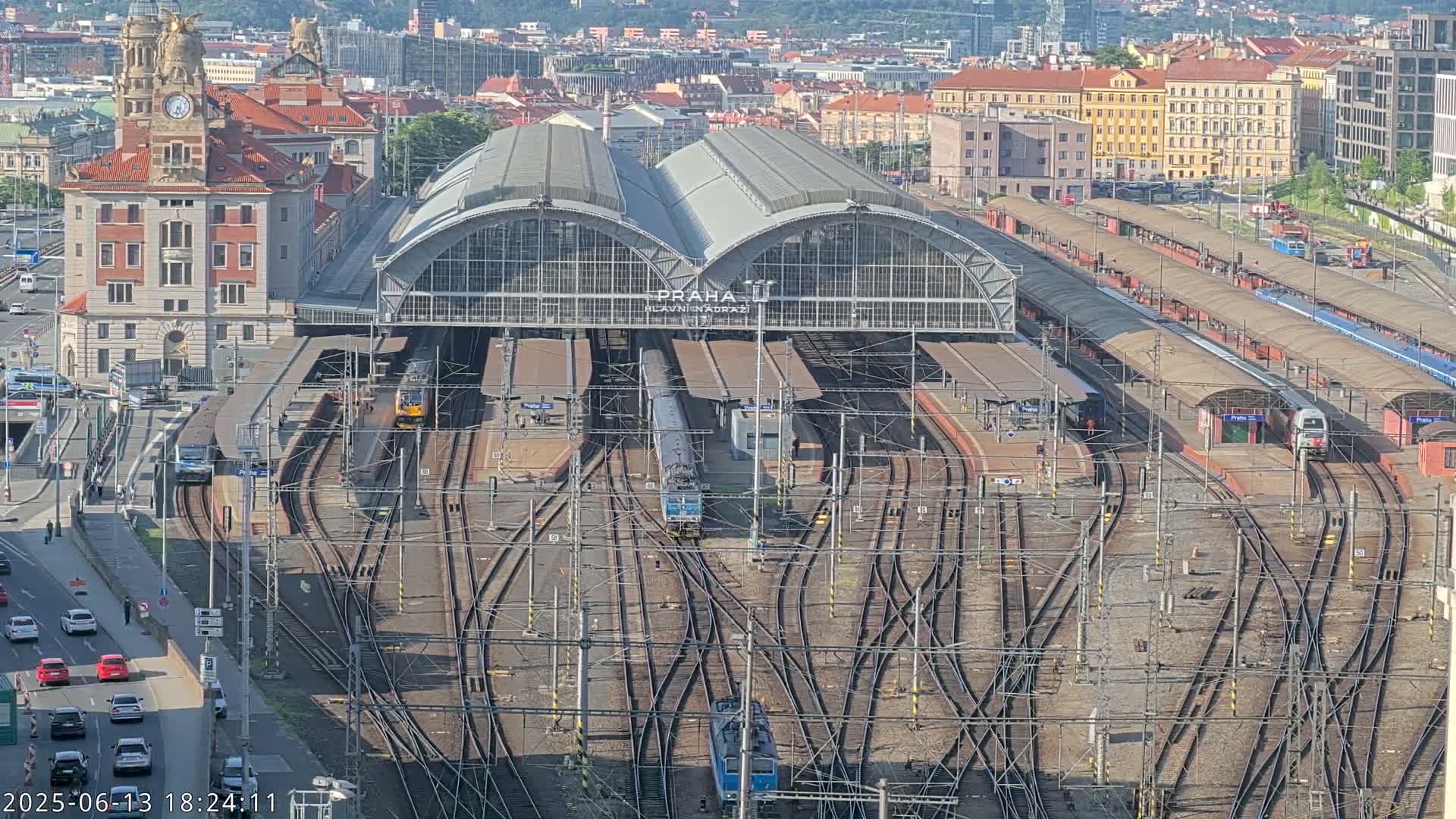 A large train station with numerous tracks and trains, viewed from above on a sunny day.