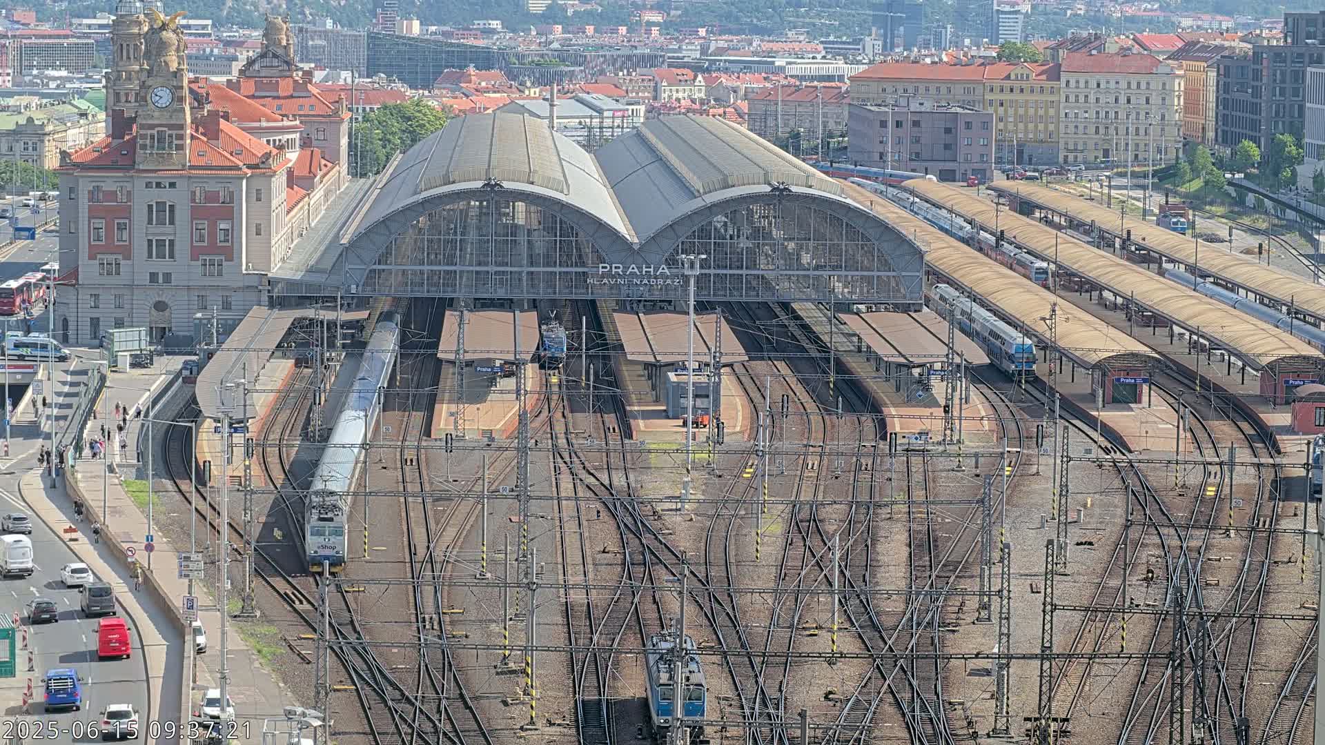 A large train station with numerous tracks and trains, under a clear sunny sky.