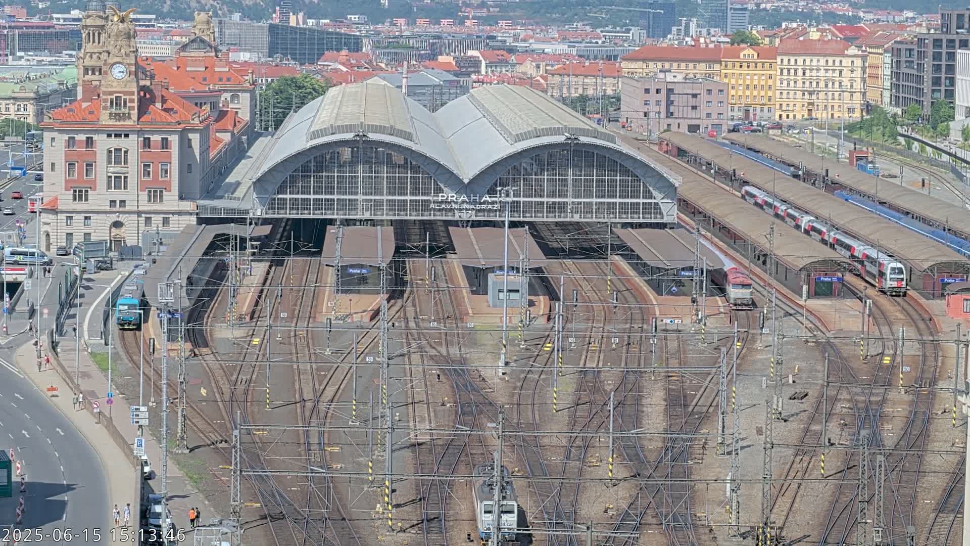 A large train station with numerous tracks and several trains, under a sunny sky.