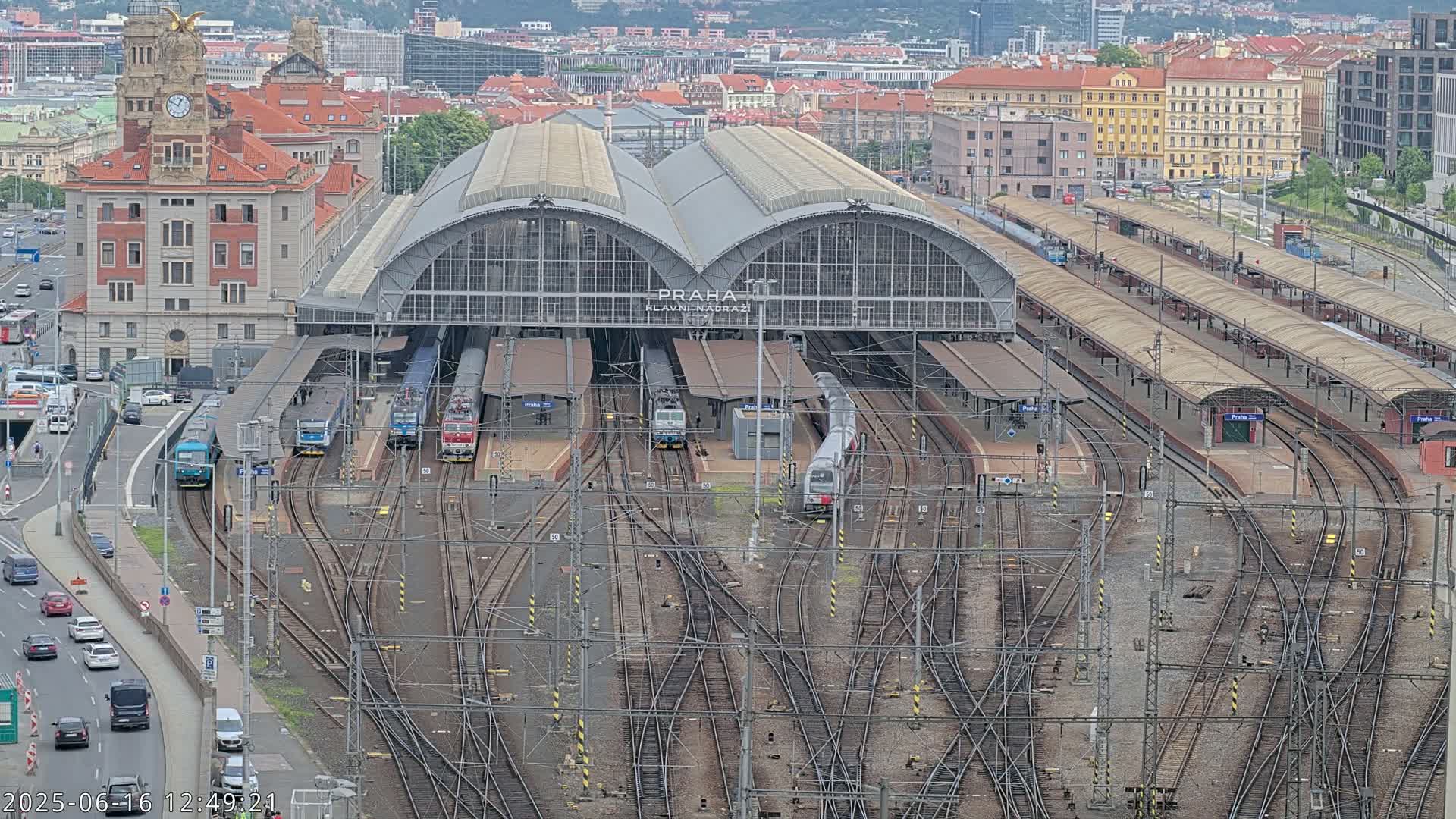 An overhead view of a large train station with numerous trains at platforms and a complex network of tracks, under an overcast sky.