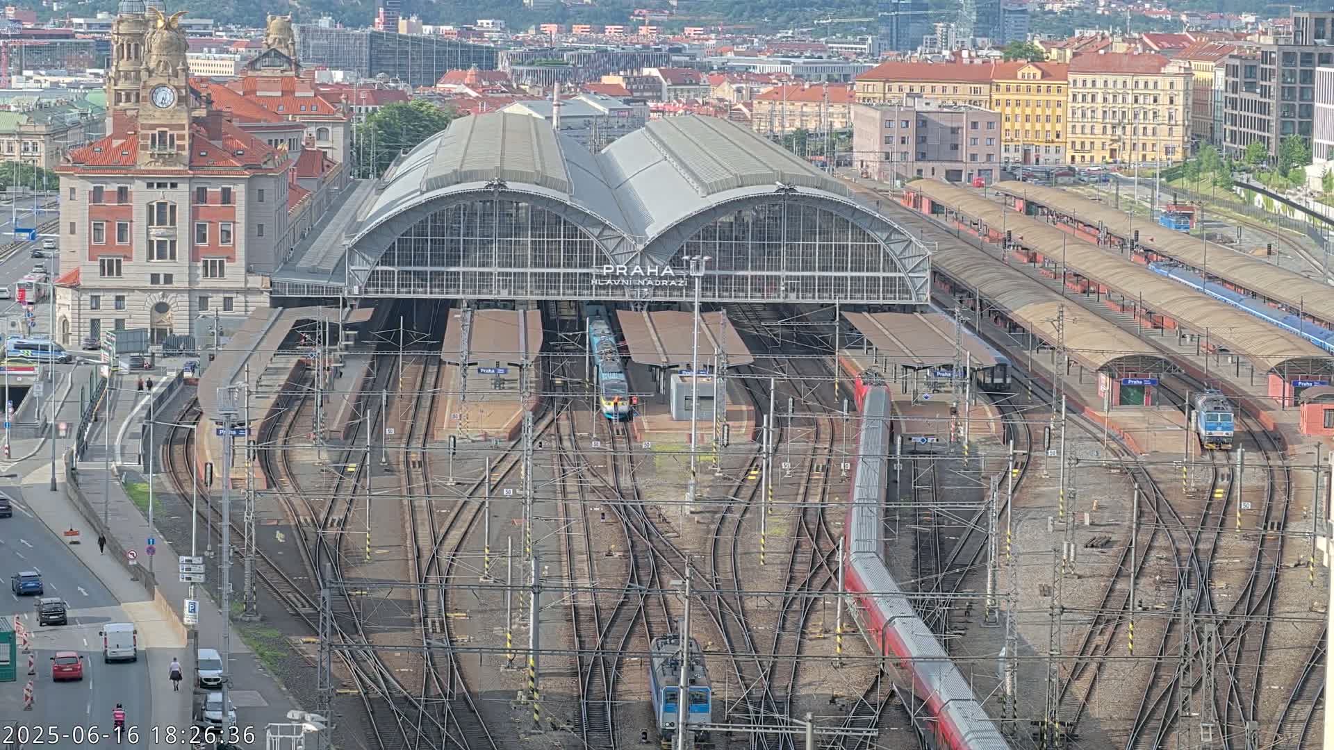 A large train station with numerous tracks and trains, surrounded by city buildings on a clear day.
