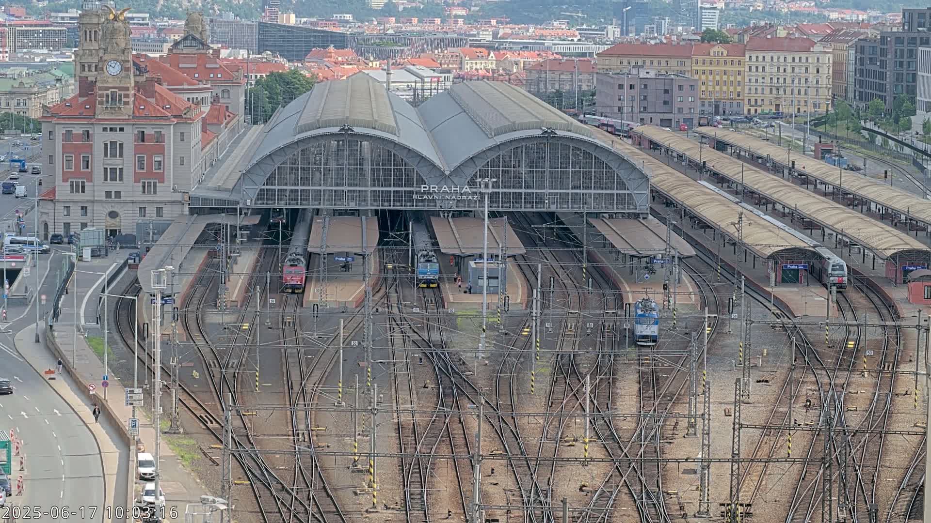 A large train station with many tracks and several trains, situated in a city on an overcast day.