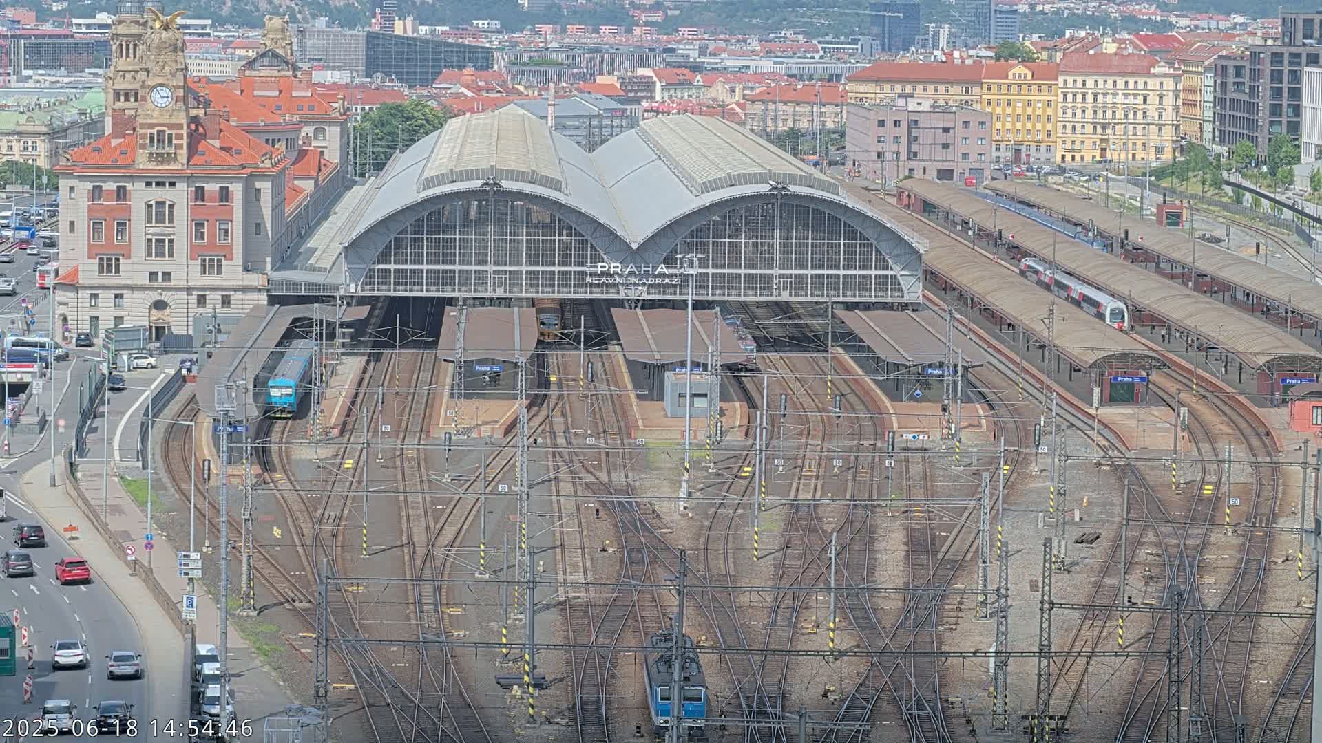 A large train station with numerous tracks and trains, viewed from above on a clear, sunny day.