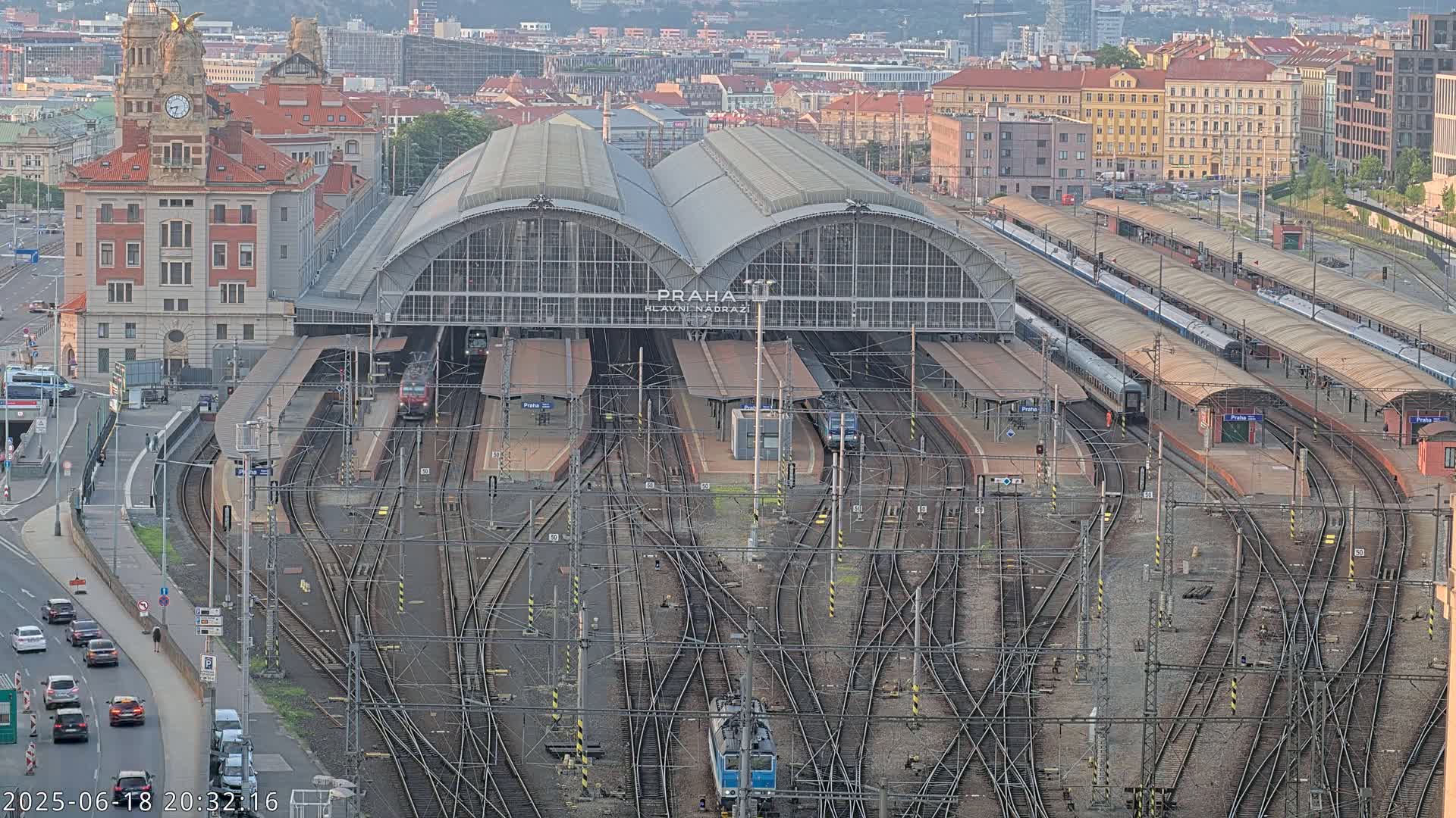 A large train station with numerous tracks and platforms, a large building, and several trains, all under a clear evening sky.