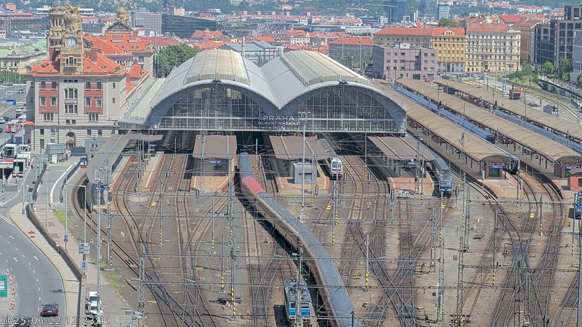 A large train station with many tracks and trains, viewed from above on a sunny day.