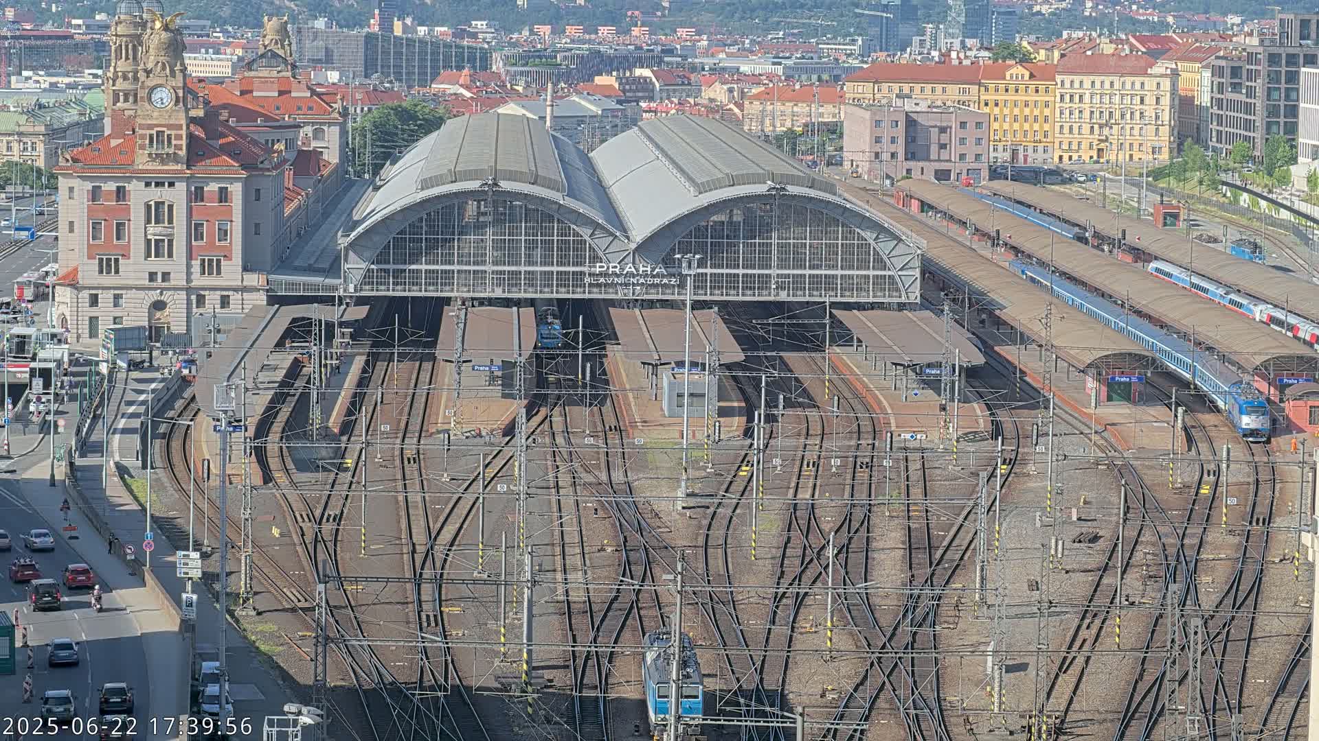 A large train station with numerous tracks and several trains, under a sunny sky.