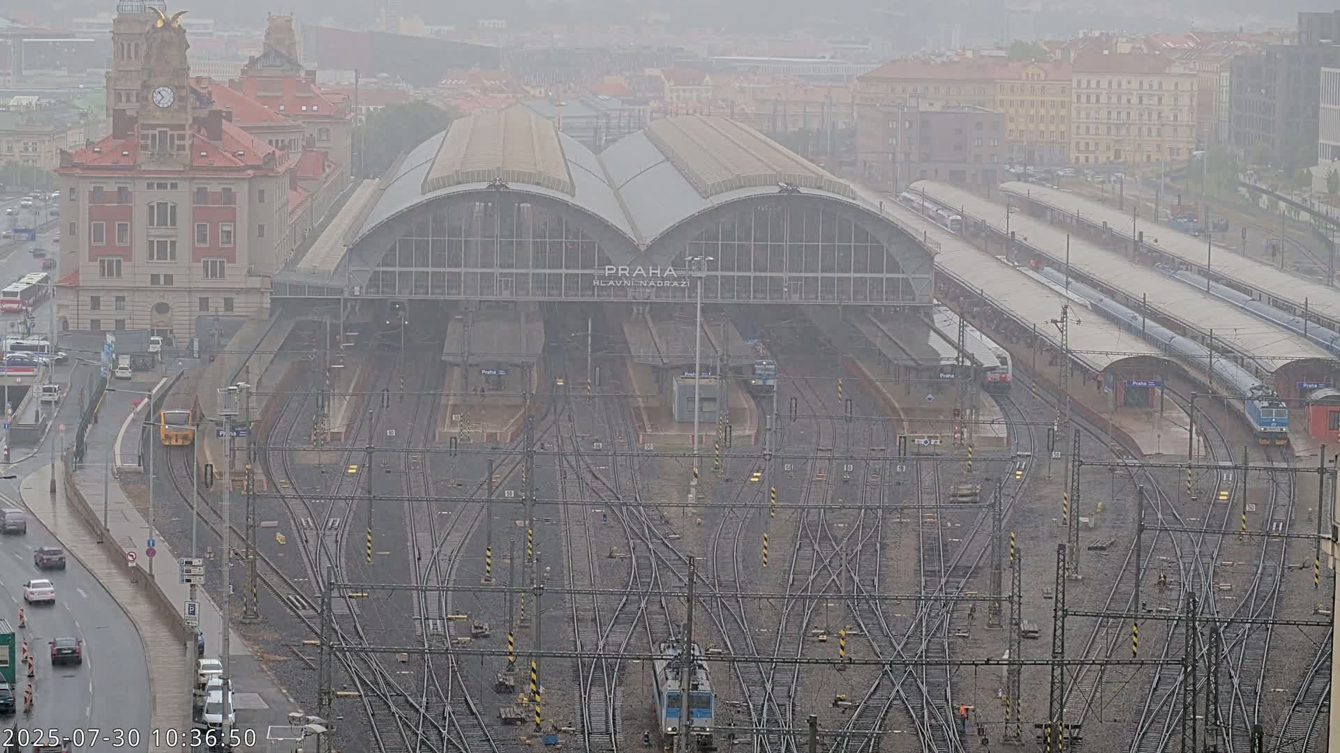 A large train station with many tracks and trains, viewed from above on a rainy day.