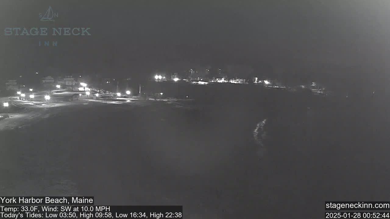 A nighttime, low-light view of a mostly dark coastline with scattered lights, under a clear sky and a southwest wind.