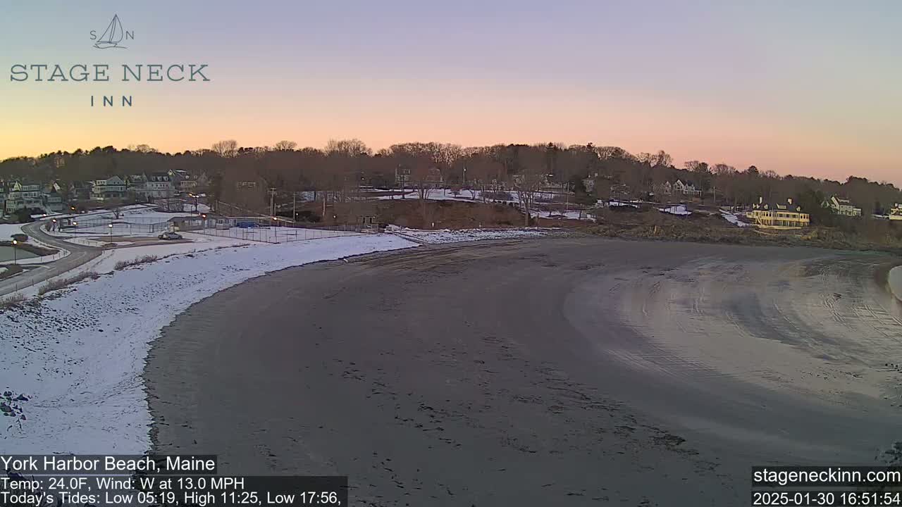 A partly snowy beach curves into a dark, wet sand expanse under a pale pink and purple twilight sky.