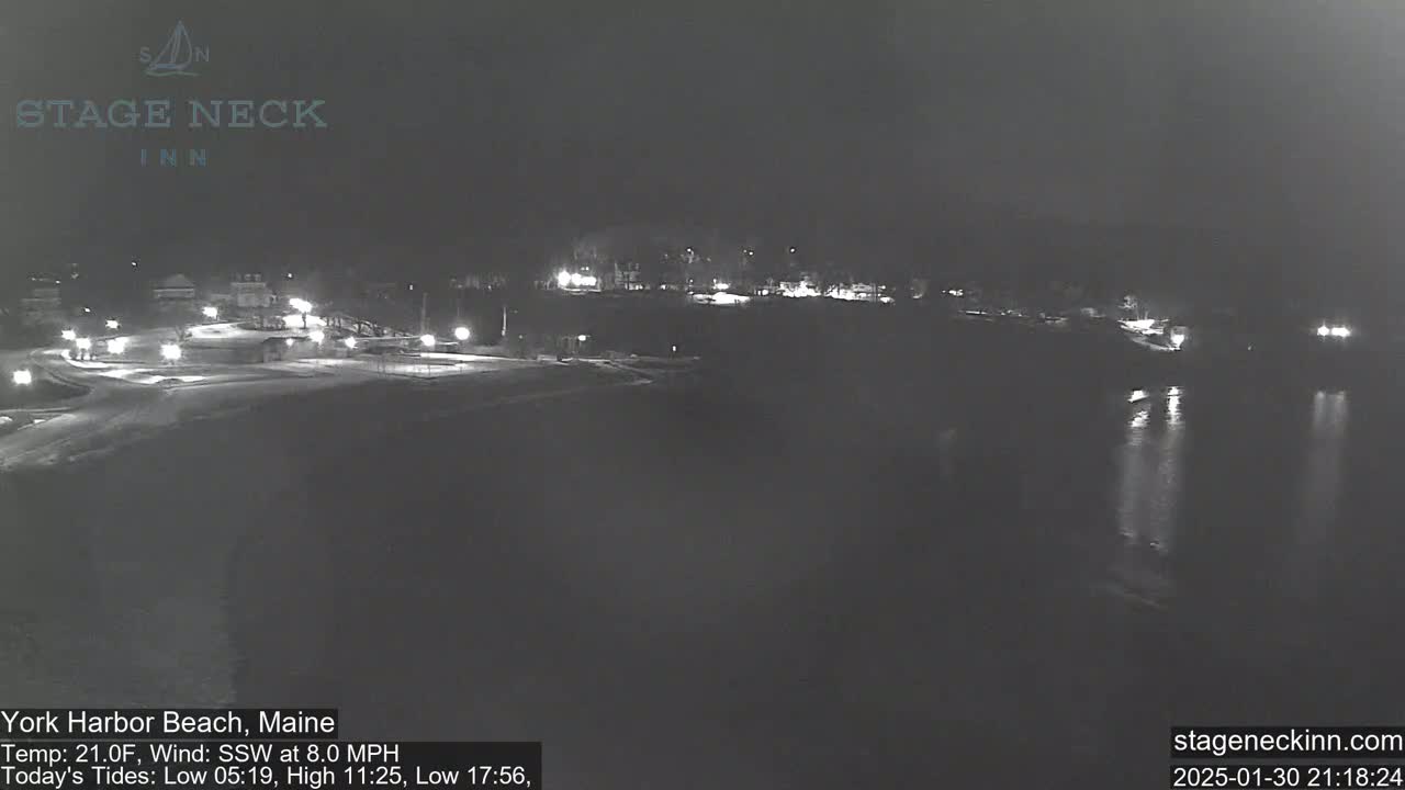 A nighttime view of a snow-covered beach and calm water under a dark sky.
