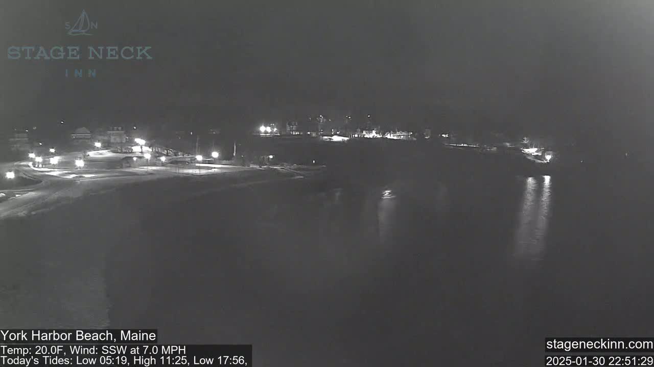 A nighttime view of a snow-covered beach and waterfront area with dim lights, under a dark sky.