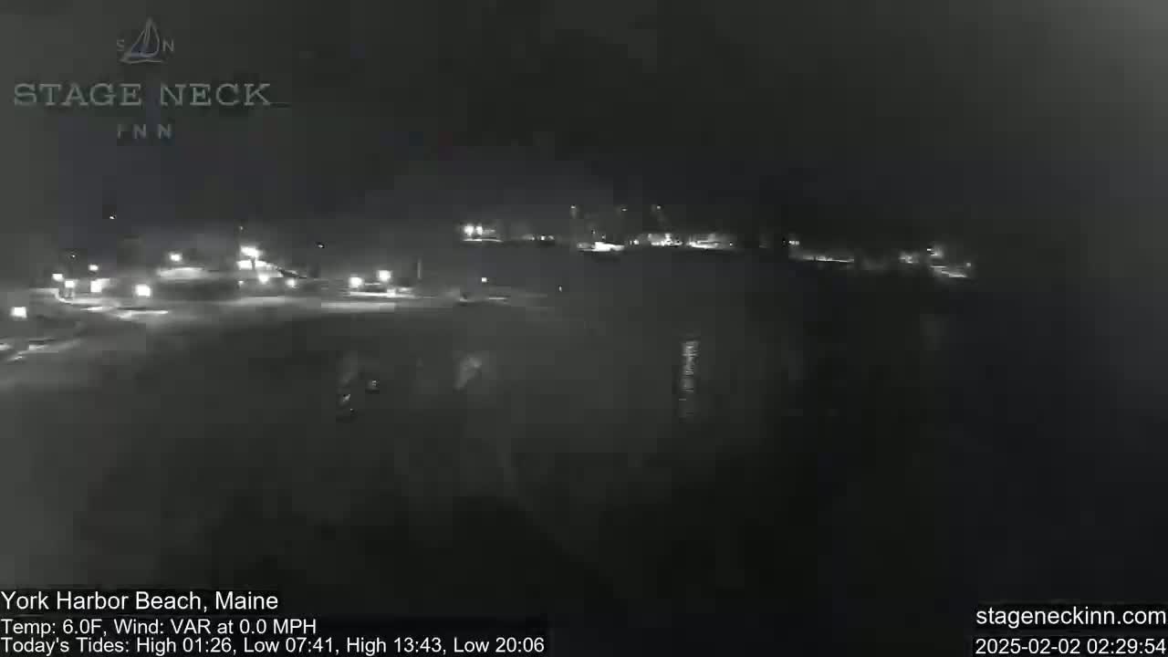A nighttime, low-light view of a mostly dark area with some distant lights, possibly a parking lot or roadside area, under a clear sky.