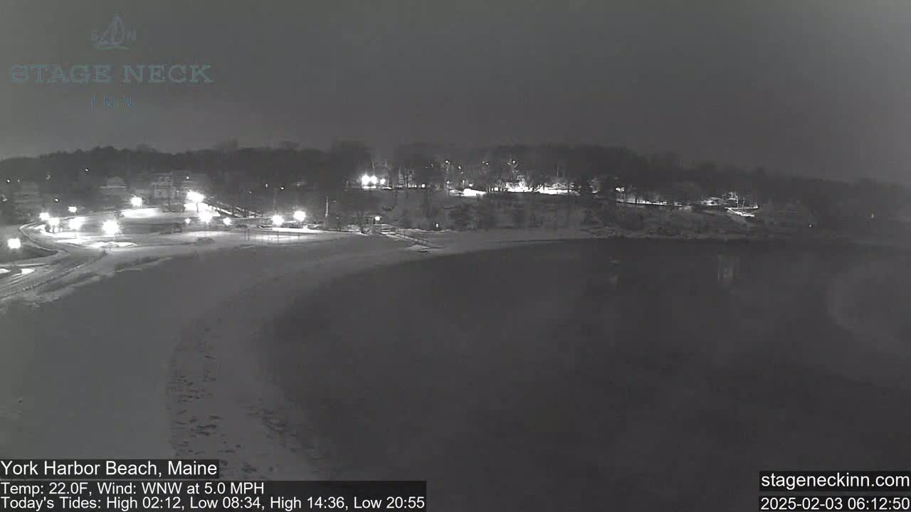 A snow-covered beach at night, under a dark sky, with a few lights visible in the distance.