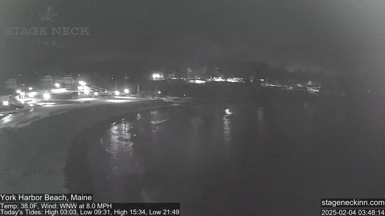 A nighttime, low-light view of a snow-covered beach and calm water under a dark sky.