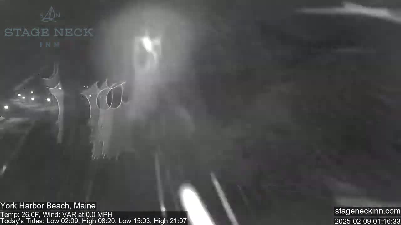 A blurry nighttime image shows heavy snow obscuring the view of a roadway.