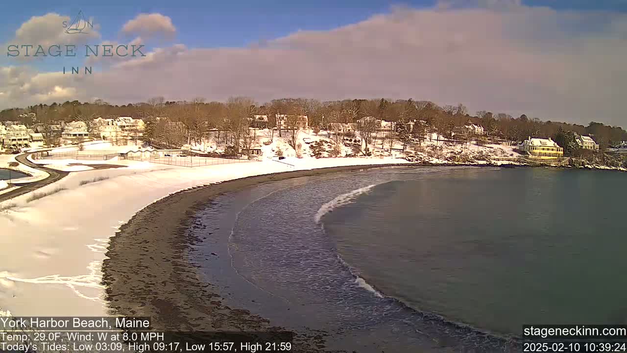 A snow-covered beach curves into a calm, dark-grey ocean under a partly sunny sky.
