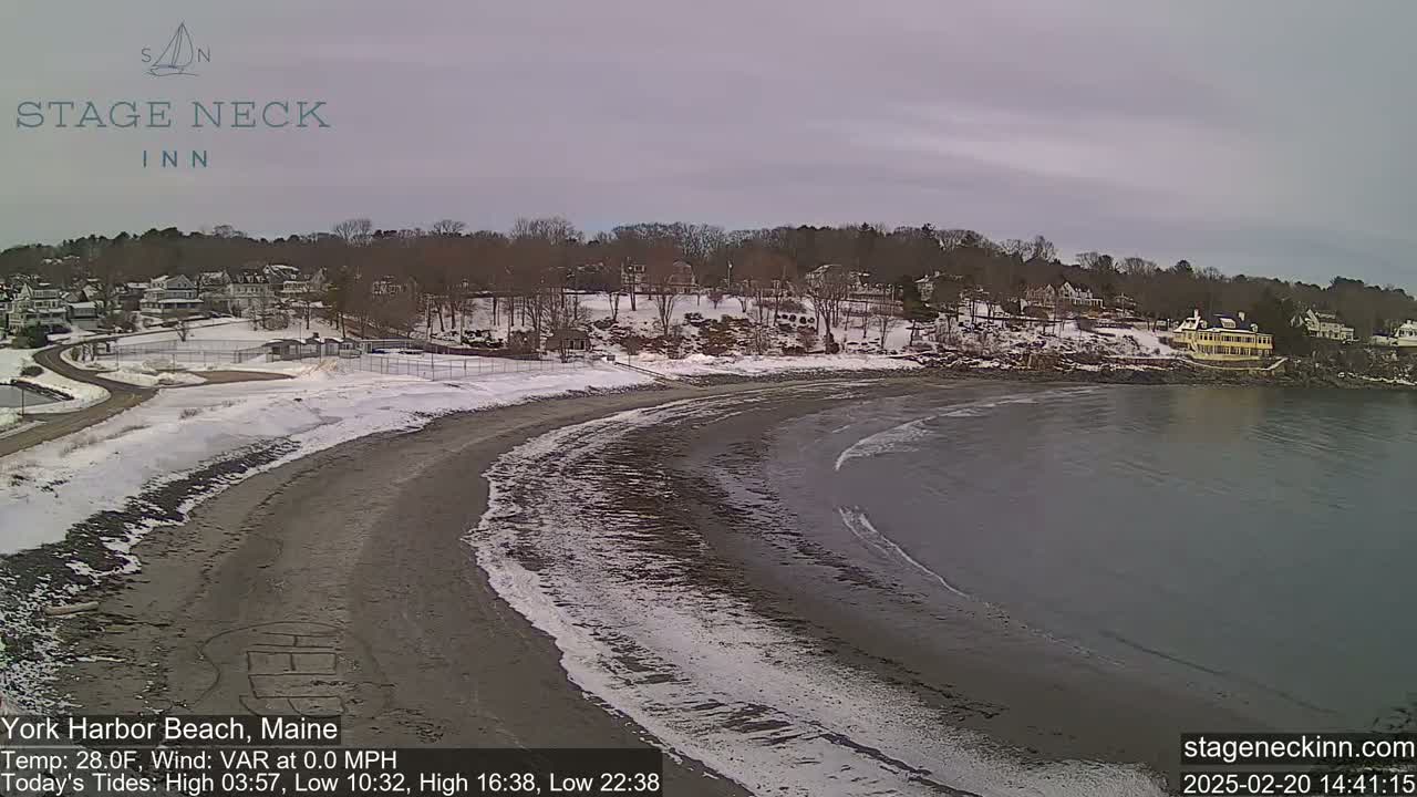A snow-covered beach curves into a calm, gray ocean under an overcast sky.