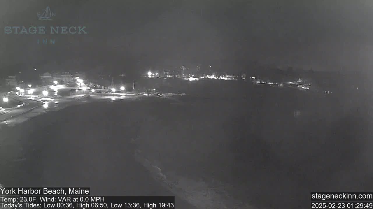 A nighttime, snow-covered coastal scene shows a dimly lit town with a few visible lights.