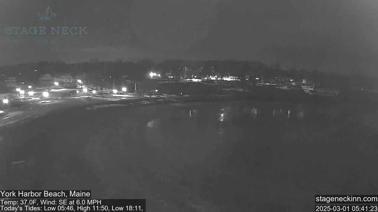 A nighttime view of a dark, calm body of water reflecting the lights of a shoreline town under a clear sky.
