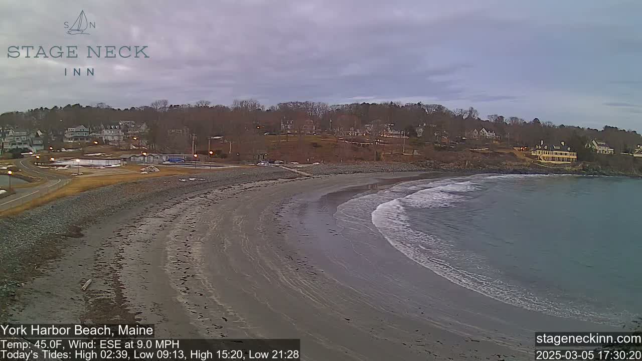 A sandy beach curves gently into a calm bay under an overcast sky.