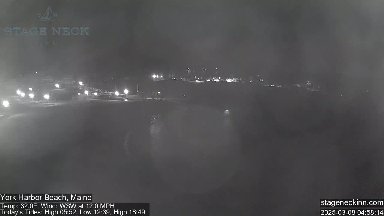 A nighttime, low-light view of a dark beach and calm water under a cloudy sky with a 12 mph wind.