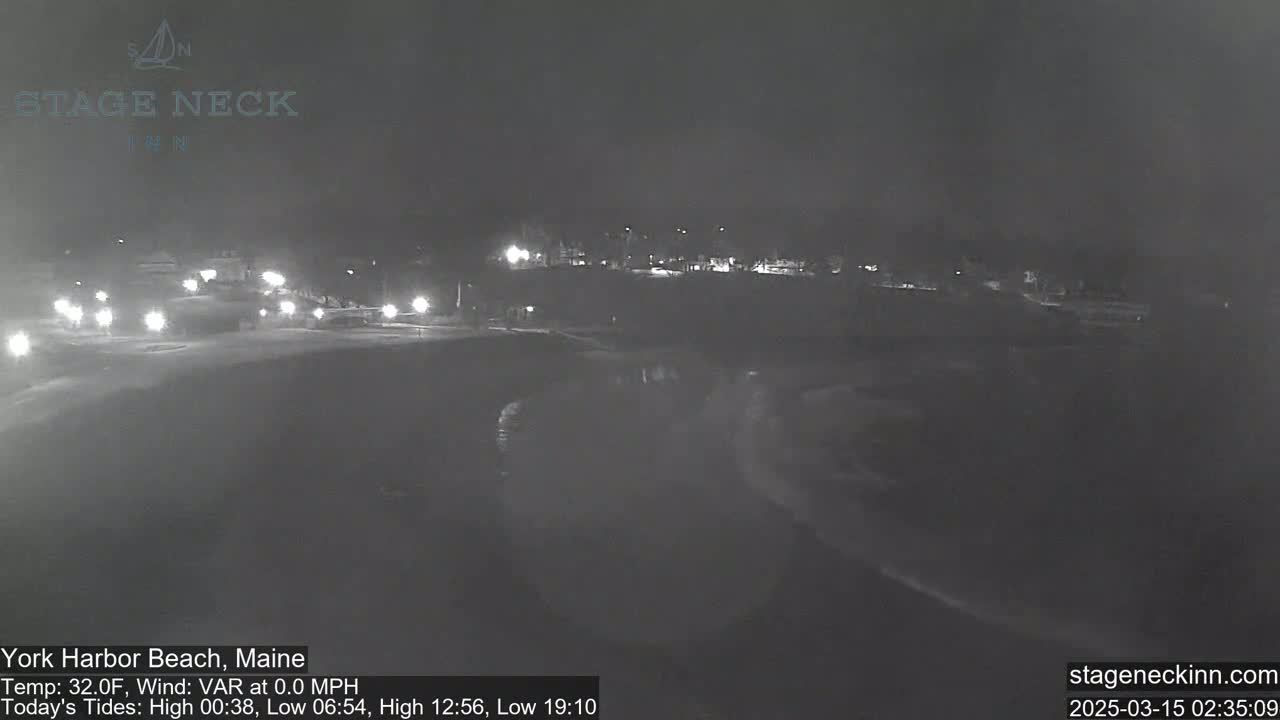 A nighttime view of a dark beach with calm waves under a cloudy sky.