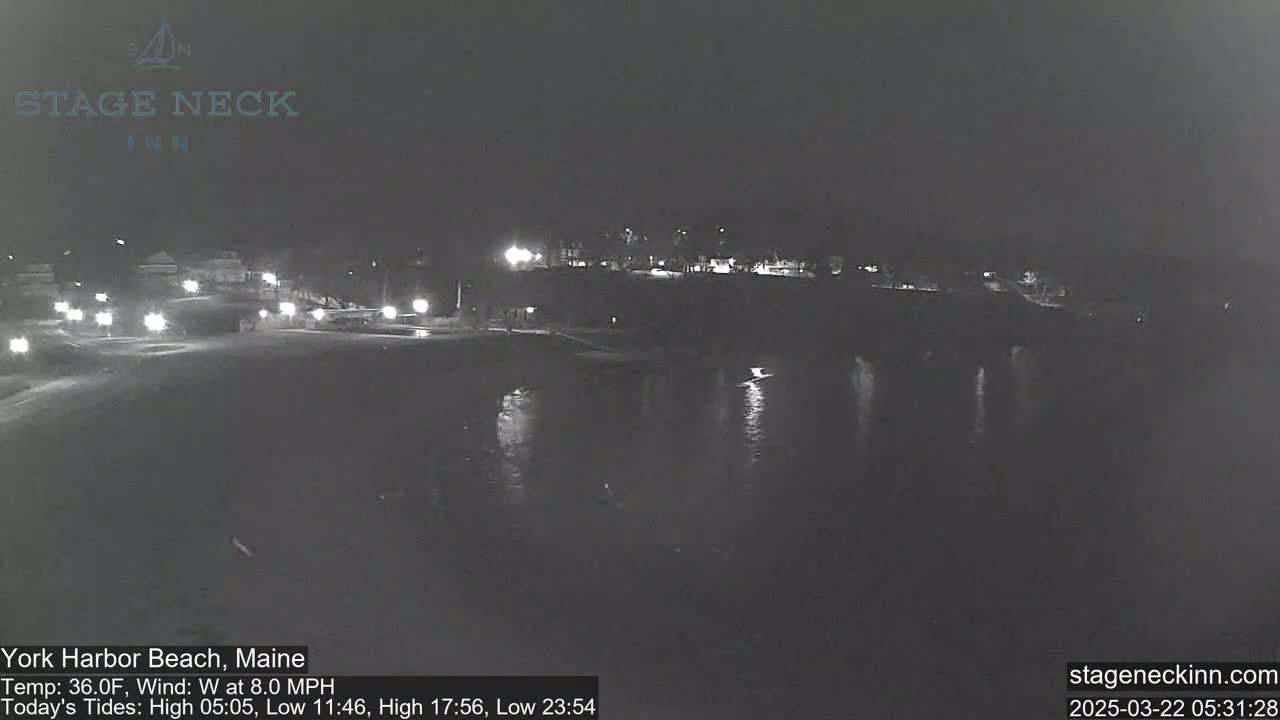 A dark nighttime scene shows a calm body of water reflecting lights from a distant shoreline.