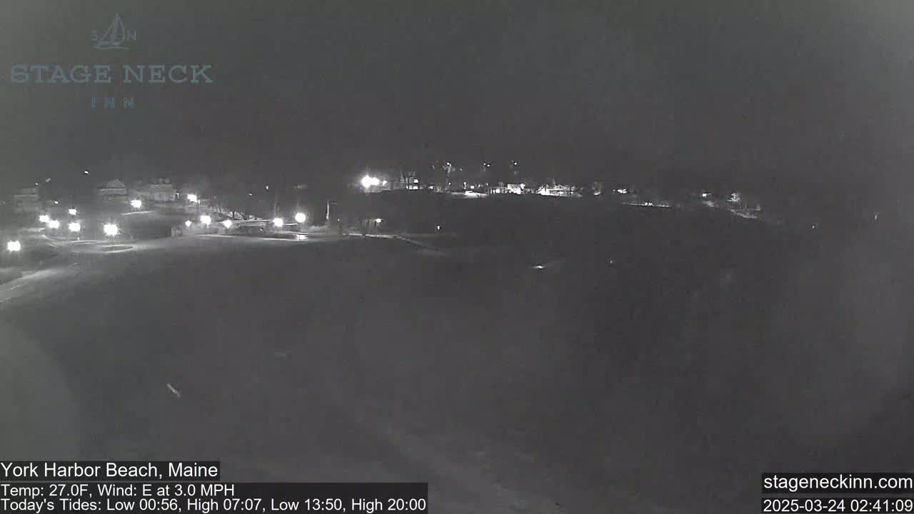 A nighttime, snow-covered parking lot with sparsely lit buildings in the background, under a clear sky and a 27°F temperature with a 3 mph east wind.
