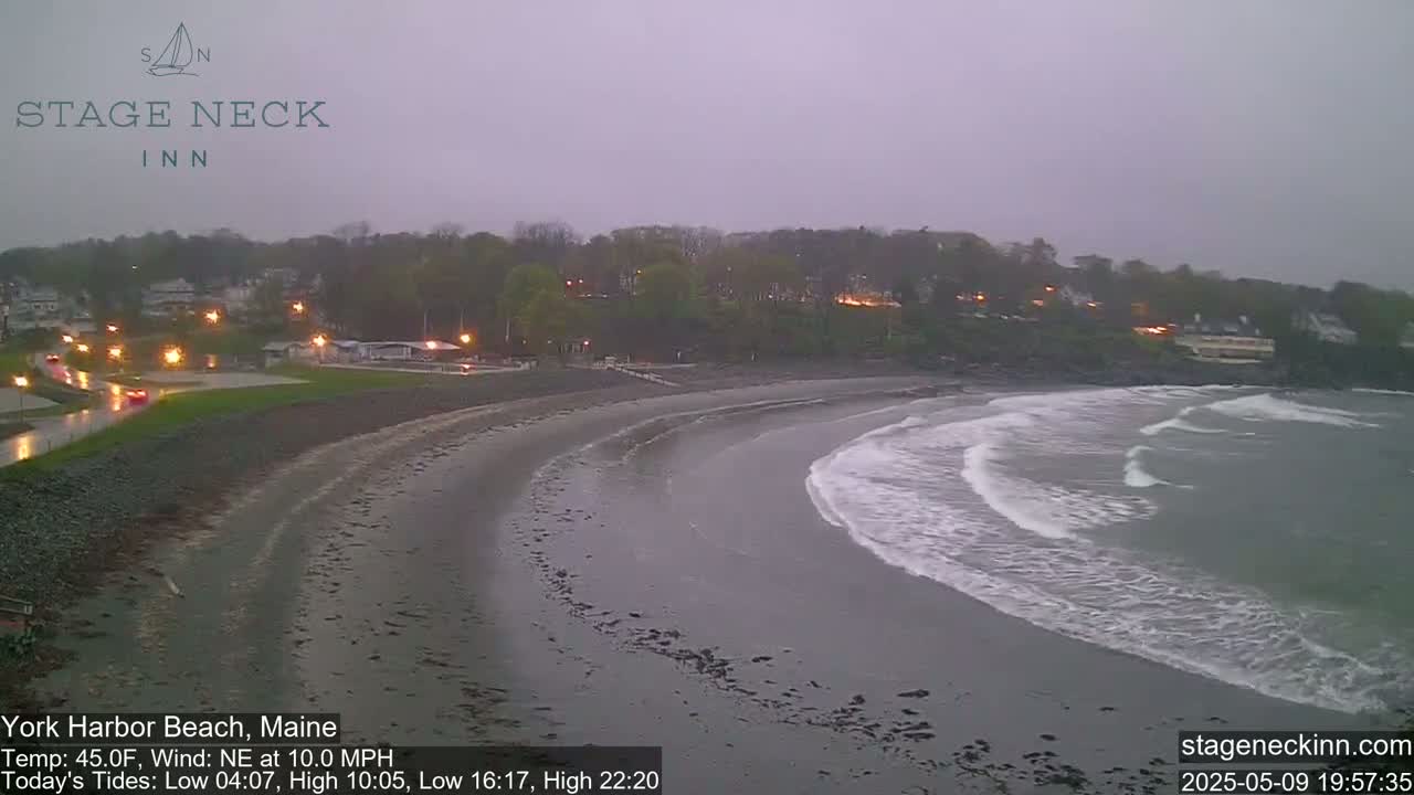 A sandy beach curves into a gray ocean with small waves under an overcast sky.