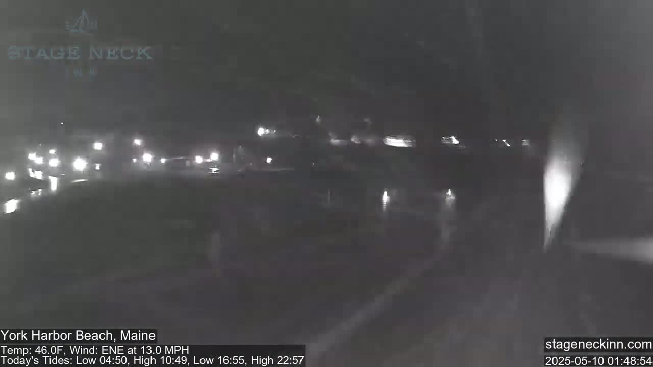 At night, under a dark sky, several vehicles with headlights on are driving on a wet road.