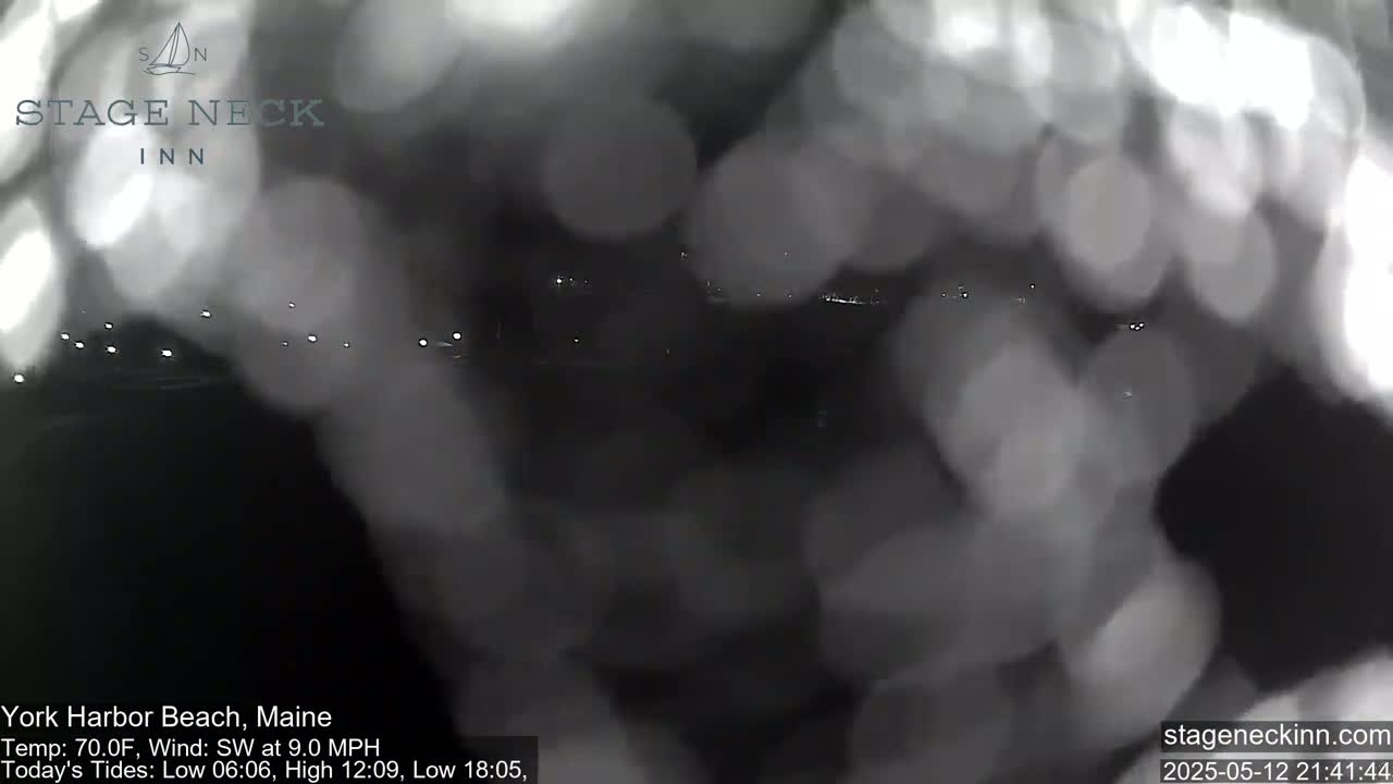 A blurry nighttime view of a dark, possibly watery area with faint lights in the distance, under a 70°F temperature with a southwest wind.