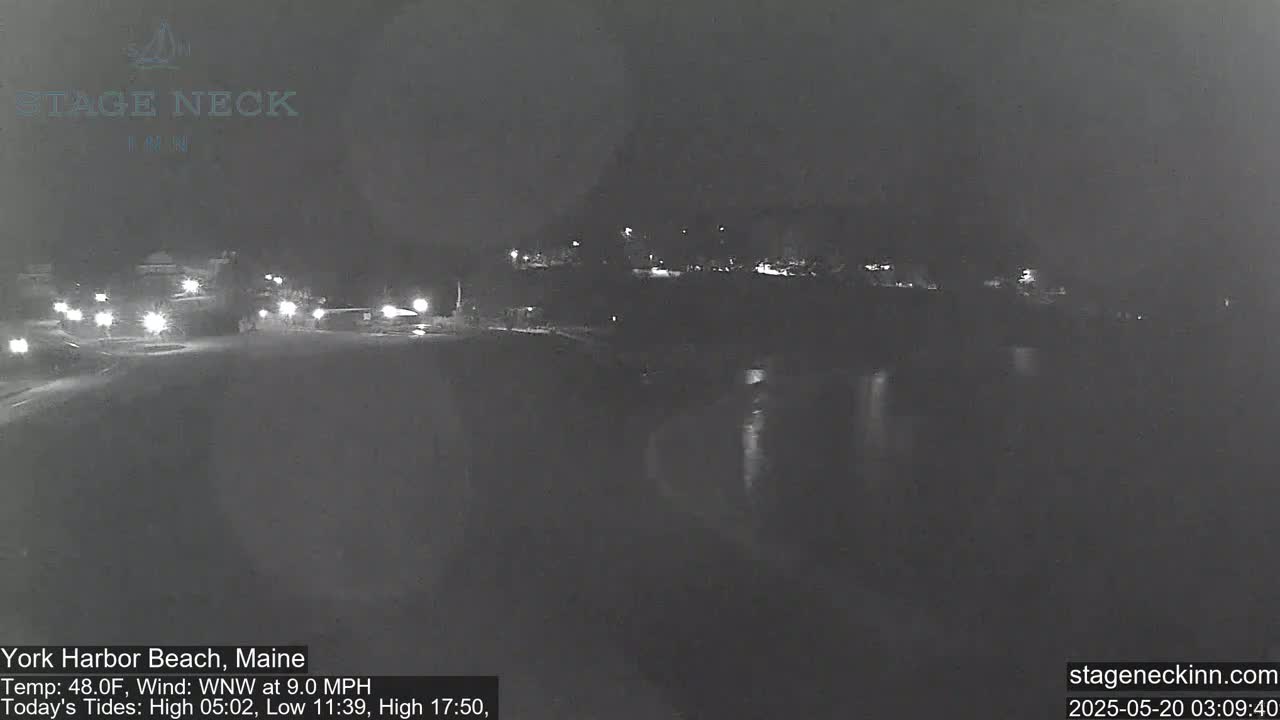 A nighttime, low-light view of a mostly empty road near a body of water, with some distant lights visible.