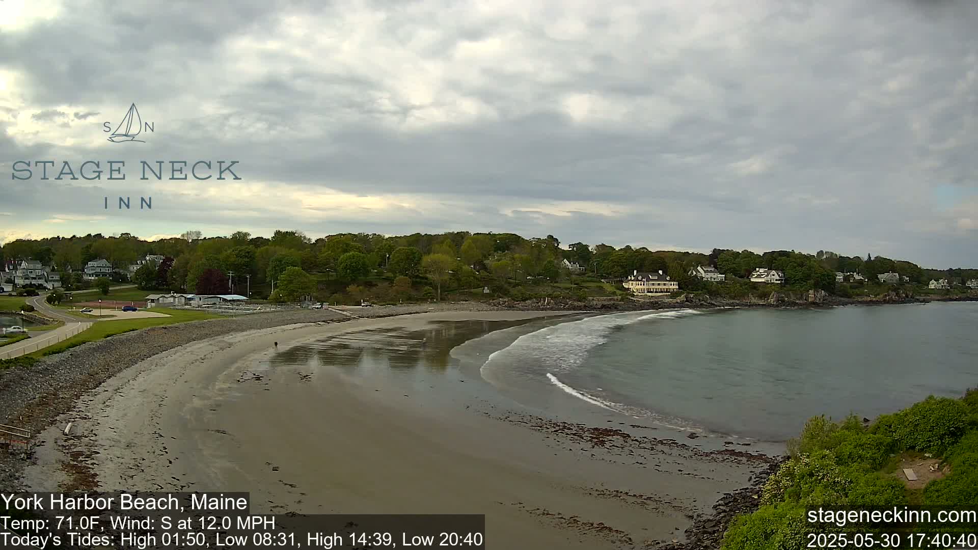 A sandy beach curves into calm, gray water under a cloudy sky.
