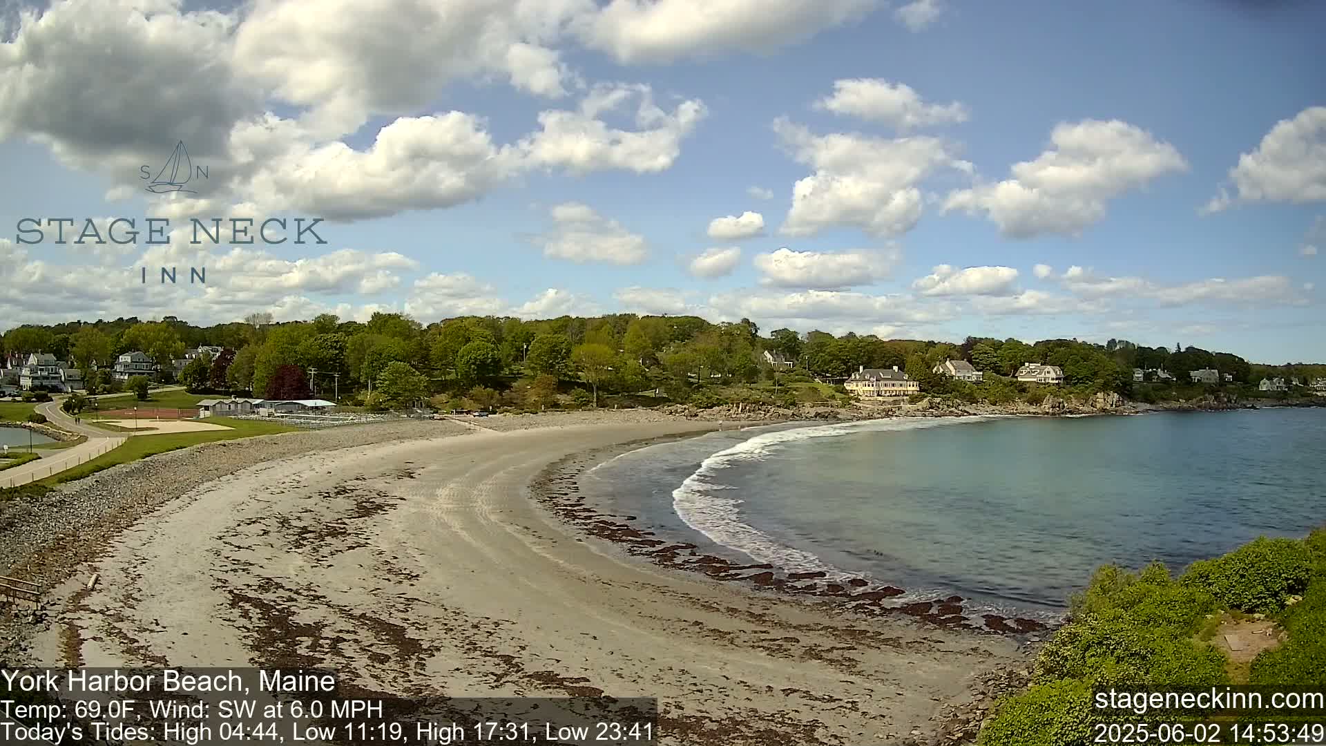 A sandy beach curves into a calm bay under a partly cloudy sky.