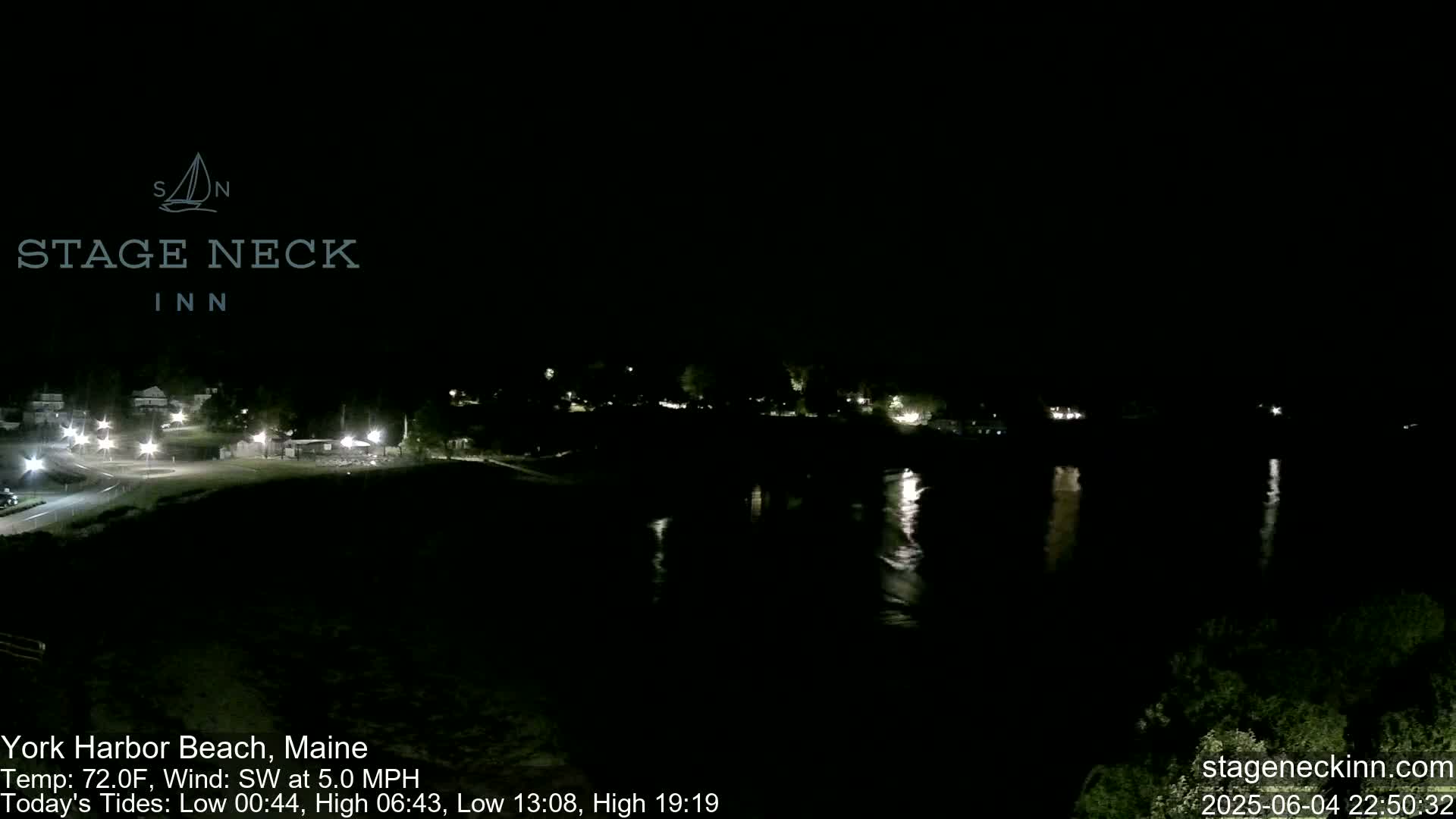 A nighttime view of a calm body of water reflecting the lights of a town across the water under a clear, dark sky.