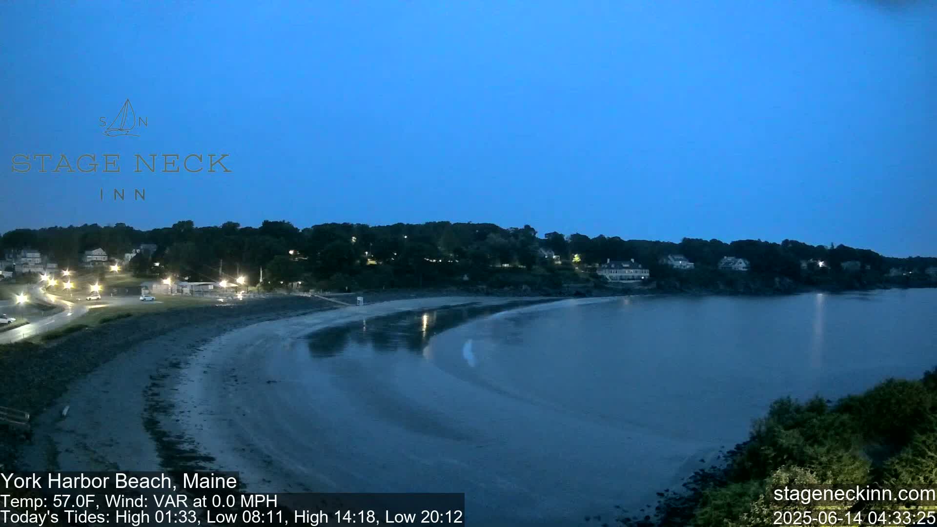 A dark, calm bay at twilight reflects the lights of a small town nestled along its shore.