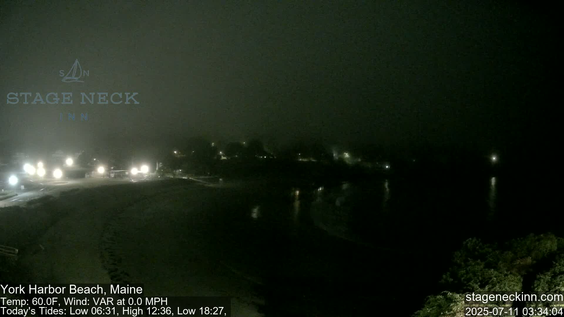 A dark, foggy nighttime scene shows a beach and calm water with a few distant lights visible.