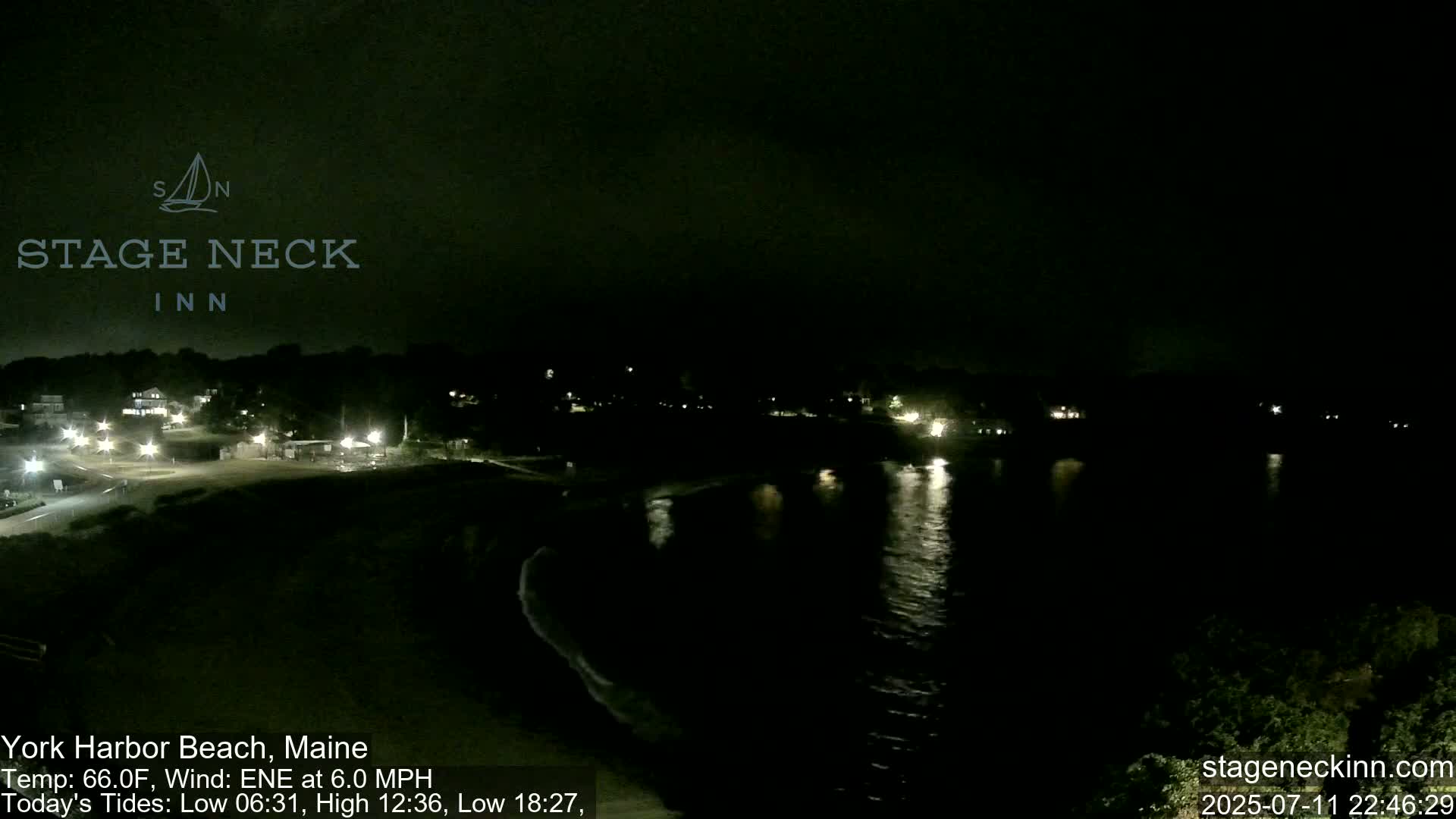 A dark, foggy nighttime scene shows a beach and calm water with a few distant lights visible.