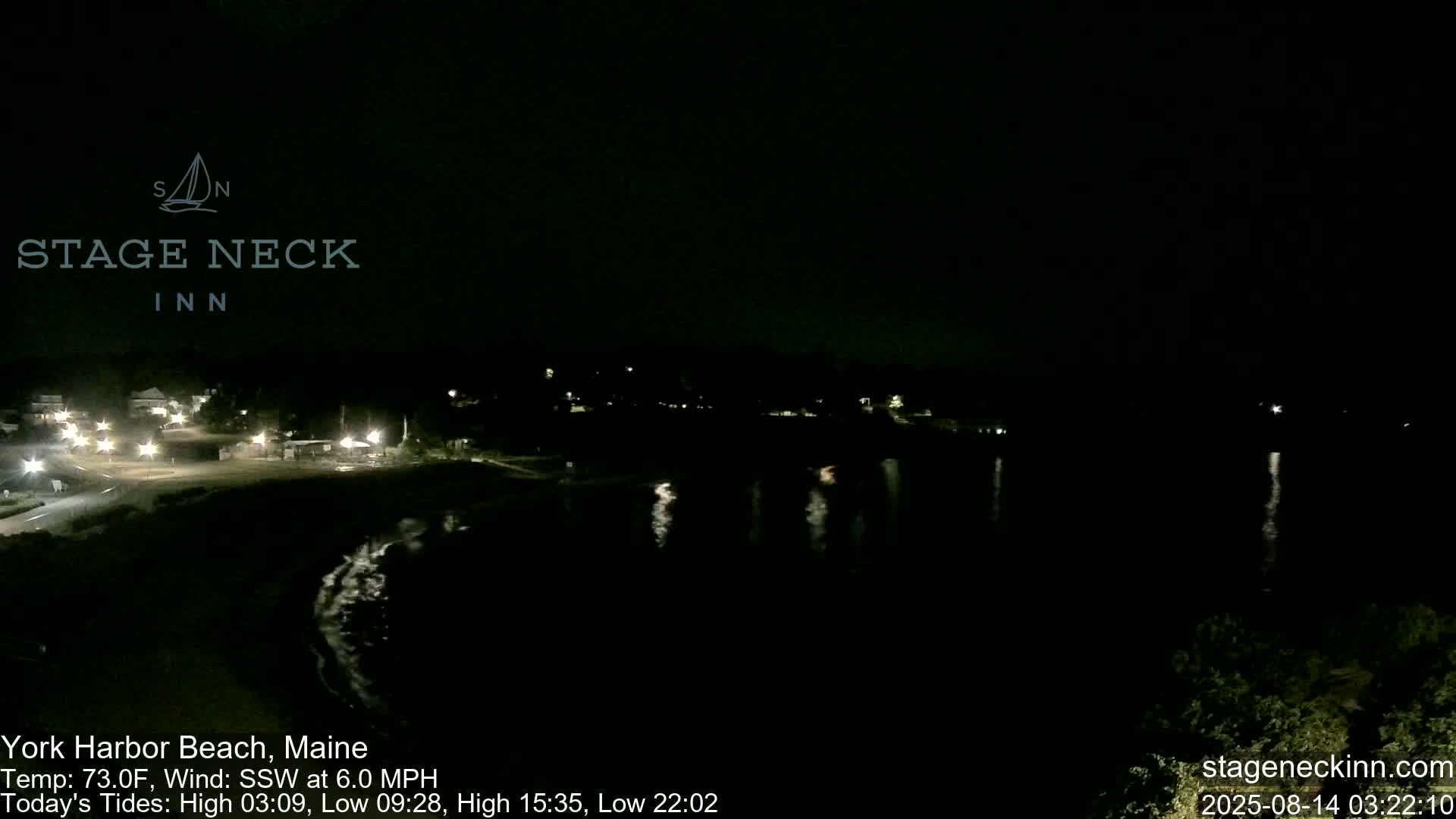 A nighttime view of a dark body of water reflecting lights from a nearby shore, under a clear sky.