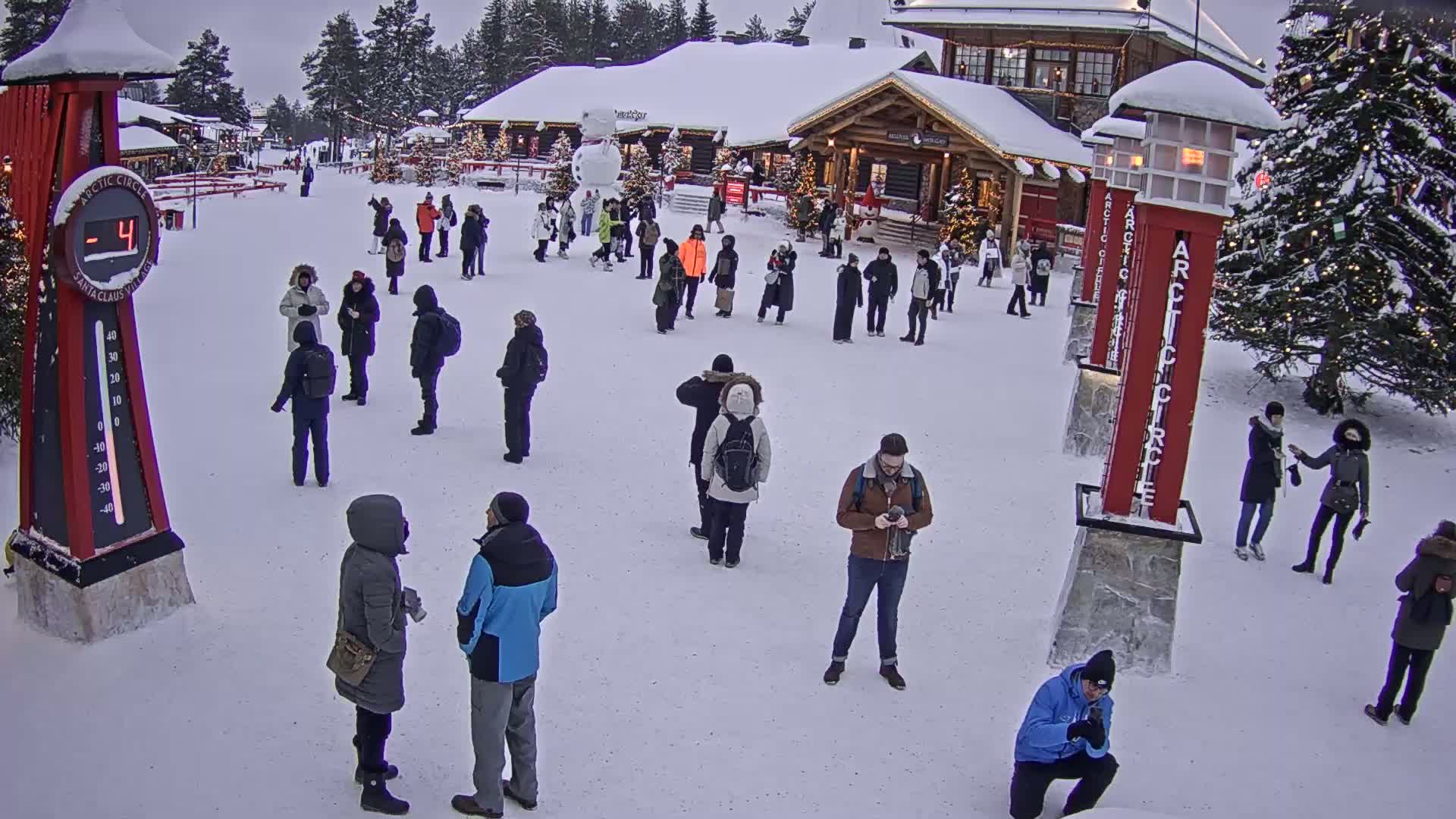 Many people are gathered in a snowy plaza in front of wooden buildings, with a thermometer displaying -4 degrees.