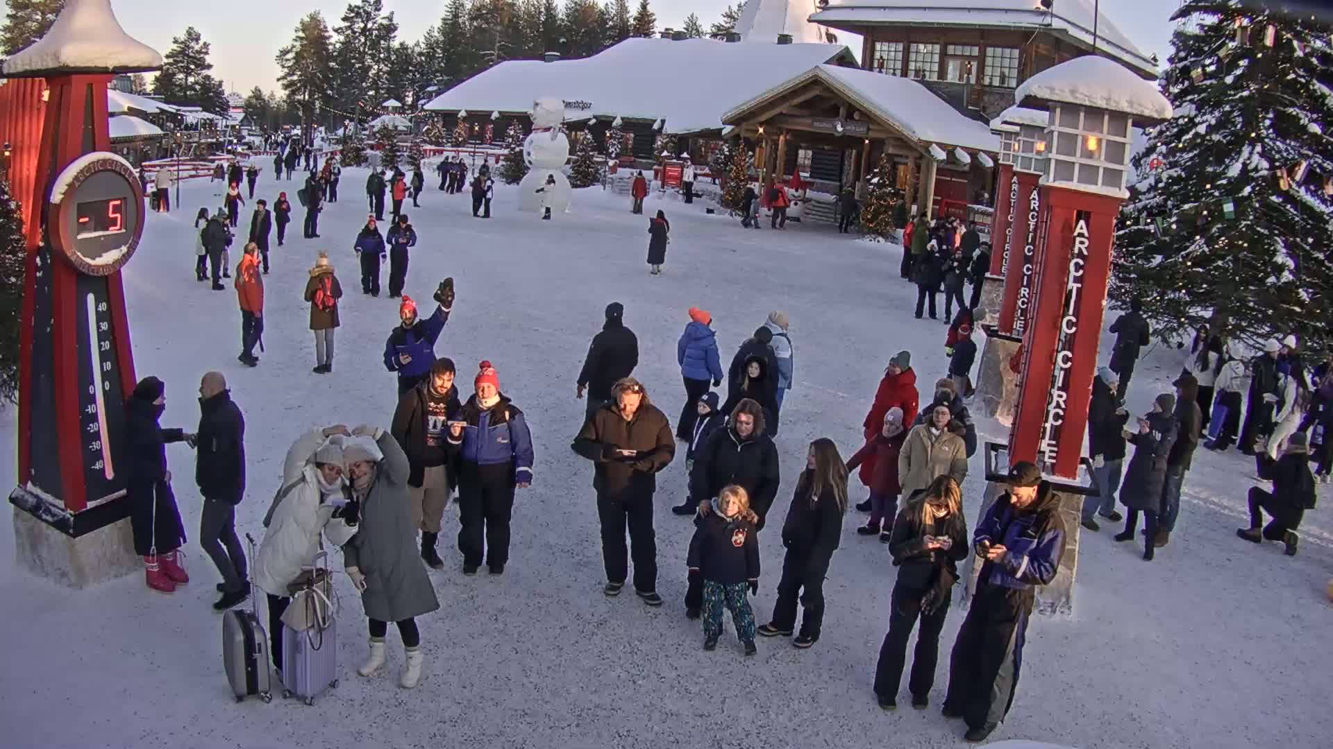 Many people are gathered in a snowy plaza in front of a building, with a large snowman nearby and a thermometer showing a temperature of -5 degrees.