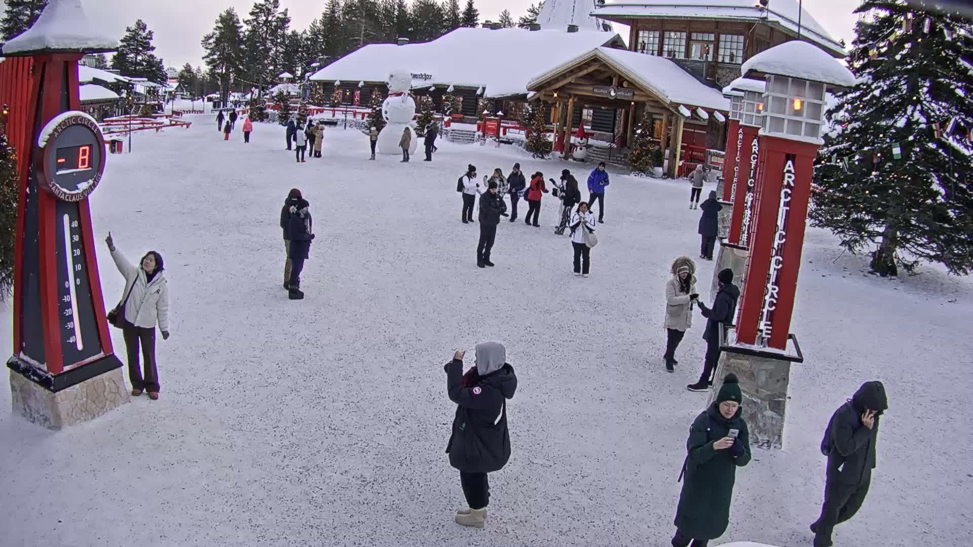 A snowy plaza with several people and a large thermometer showing -8 degrees, near a building with Christmas decorations.