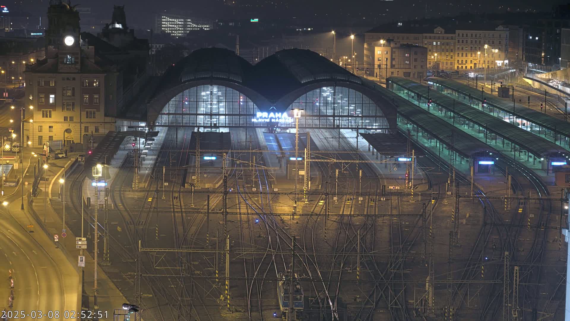 A large, illuminated train station at night, surrounded by numerous train tracks and platforms.