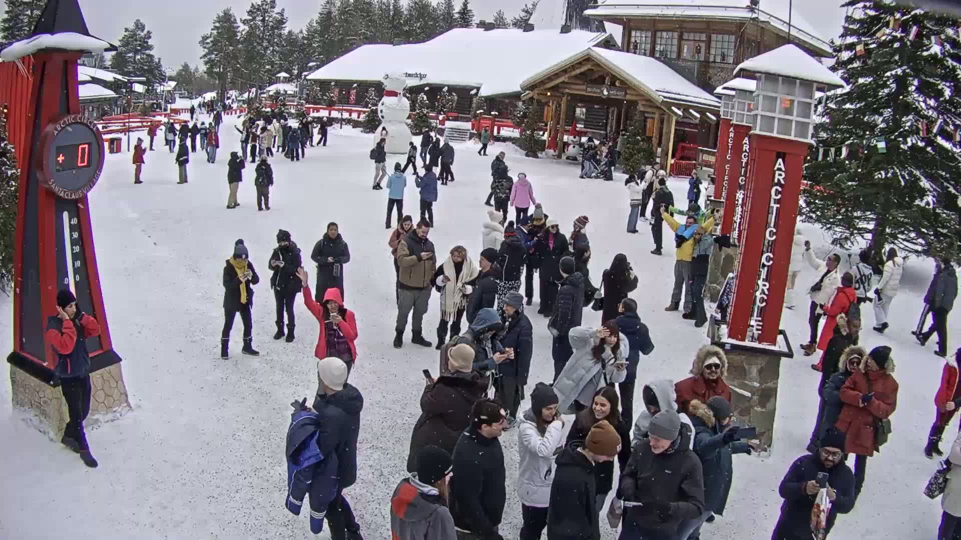 A large crowd of people gathers in a snowy plaza in front of wooden buildings, with a large snowman visible in the mid-ground.
