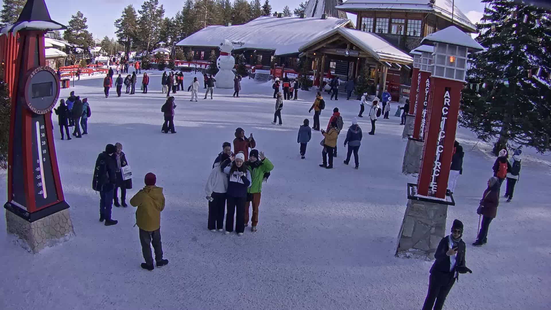 A snowy outdoor scene shows many people gathered in a plaza in front of a building, with a large snowman nearby.