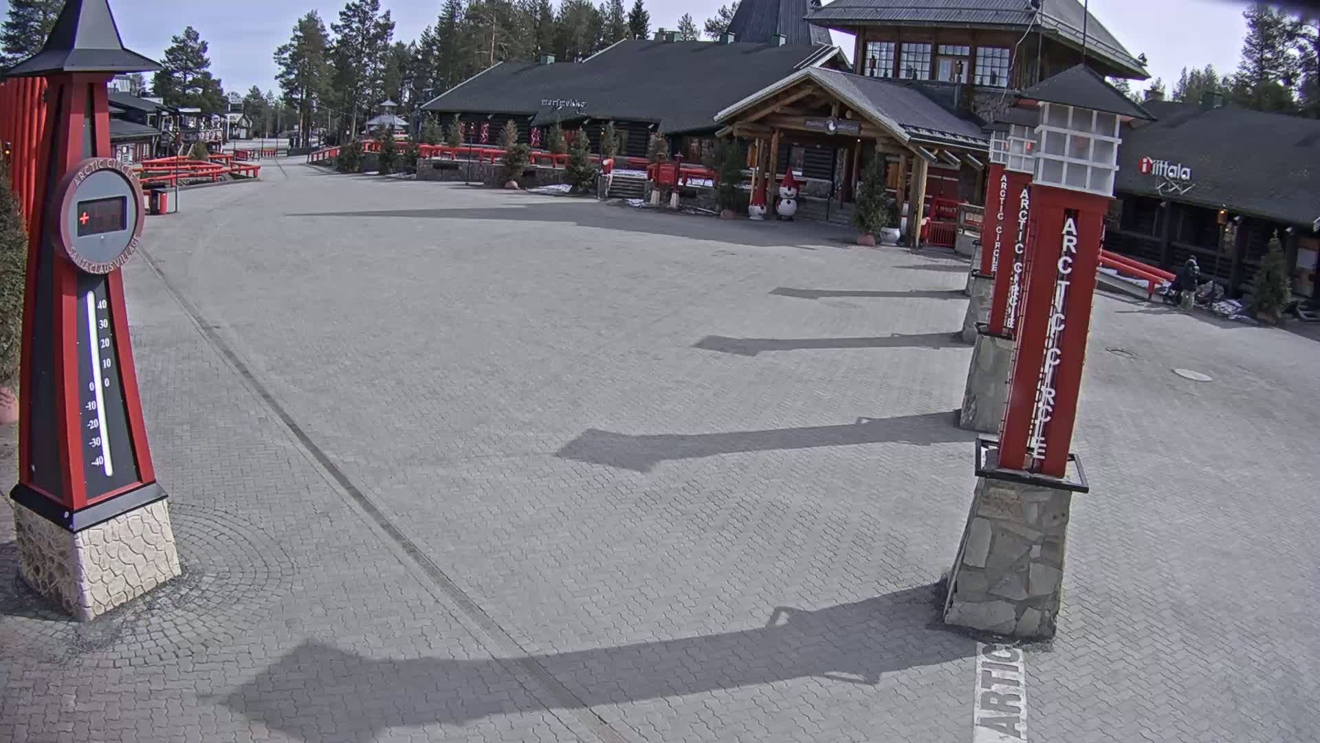 A paved plaza with a large building and several red pillars stands under a sunny sky.