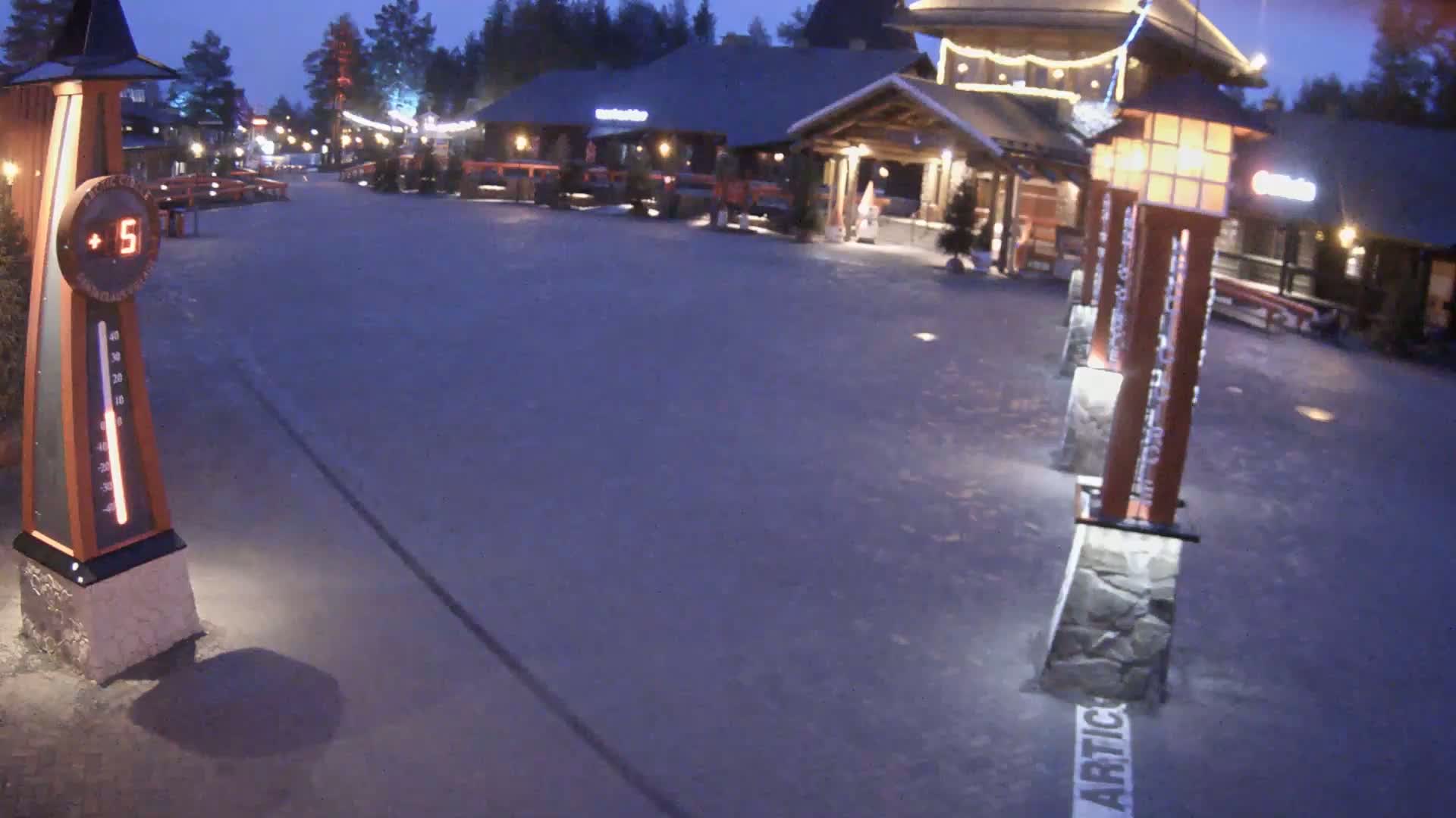 A nighttime, outdoor view of a paved plaza with several buildings in the background, illuminated by lights, and a thermometer showing a temperature of 5 degrees.
