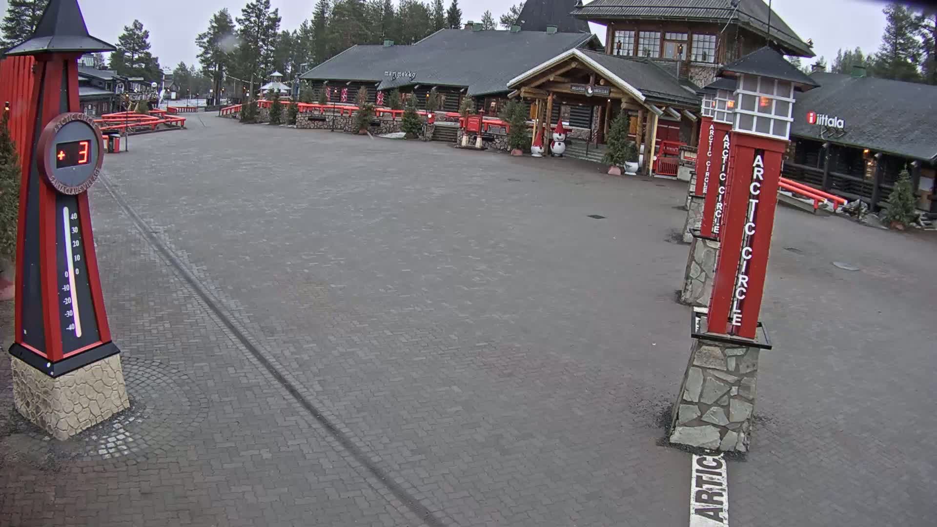 A brick paved plaza with several red and gray Arctic Circle markers and a large thermometer displaying 3 degrees, under an overcast sky.